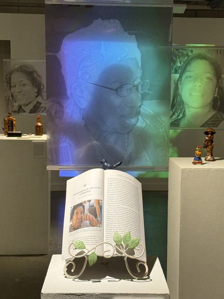 Exhibition view from Invisible Identities, featuring suspended images and personal objects.